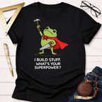 Black cotton tee with a frog in a red cape holding a hammer and saw, "I Build Stuff. What's Your Superpower?" text. Women's funny woodworking graphic tee shirt for female woodworkers, makers, and DIY builders — Sawdust & Ponytails