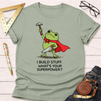 Sage green women's funny woodworking graphic tee with a superhero frog holding a hammer and saw, "I Build Stuff. What's Your Superpower?" text. Sawdust & Ponytails.