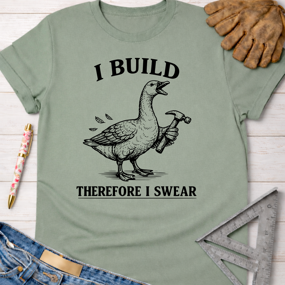 Women's funny woodworking graphic tee shirt for female woodworkers, makers, and DIY builders — Sawdust & Ponytails. Sage green cotton tee with a goose holding a hammer and "I BUILD THEREFORE I SWEAR" text.