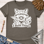 Women's funny woodworking graphic tee shirt for female woodworkers, makers, and DIY builders — Sawdust & Ponytails. Dark gray cotton tee with a white raccoon holding a drill and saw, "I Build Things" text.