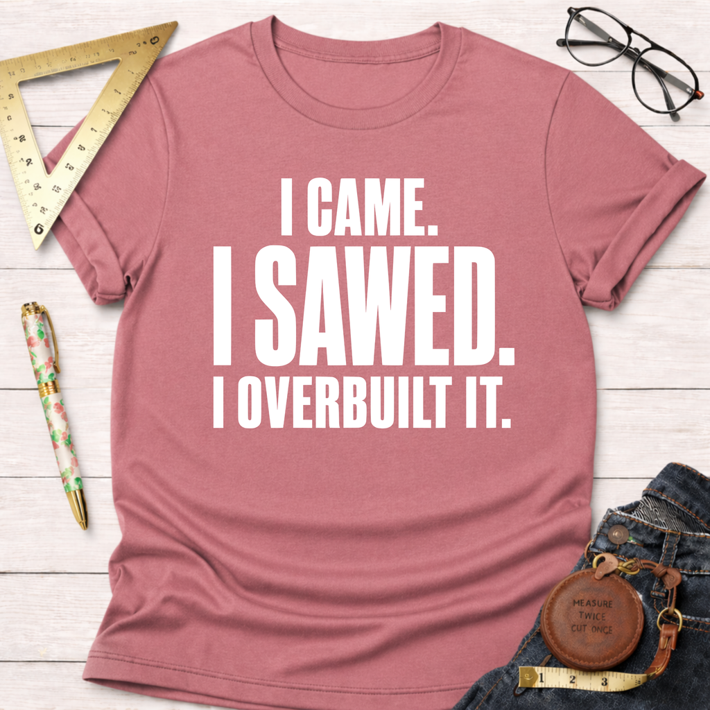 Mauve t-shirt with "I CAME. I SAWED. I OVERBUILT IT." in white text, styled with jeans and tools.