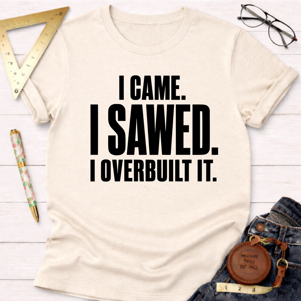 Cream t-shirt with "I CAME. I SAWED. I OVERBUILT IT." in bold black text, styled with jeans and tools.