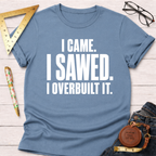 Blue "I Came. I Sawed. I Overbuilt It." t-shirt with rolled sleeves, laid flat on a white wooden surface.