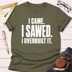 Olive green "I Came. I Sawed. I Overbuilt It." t-shirt with white text, styled on a white wooden surface.