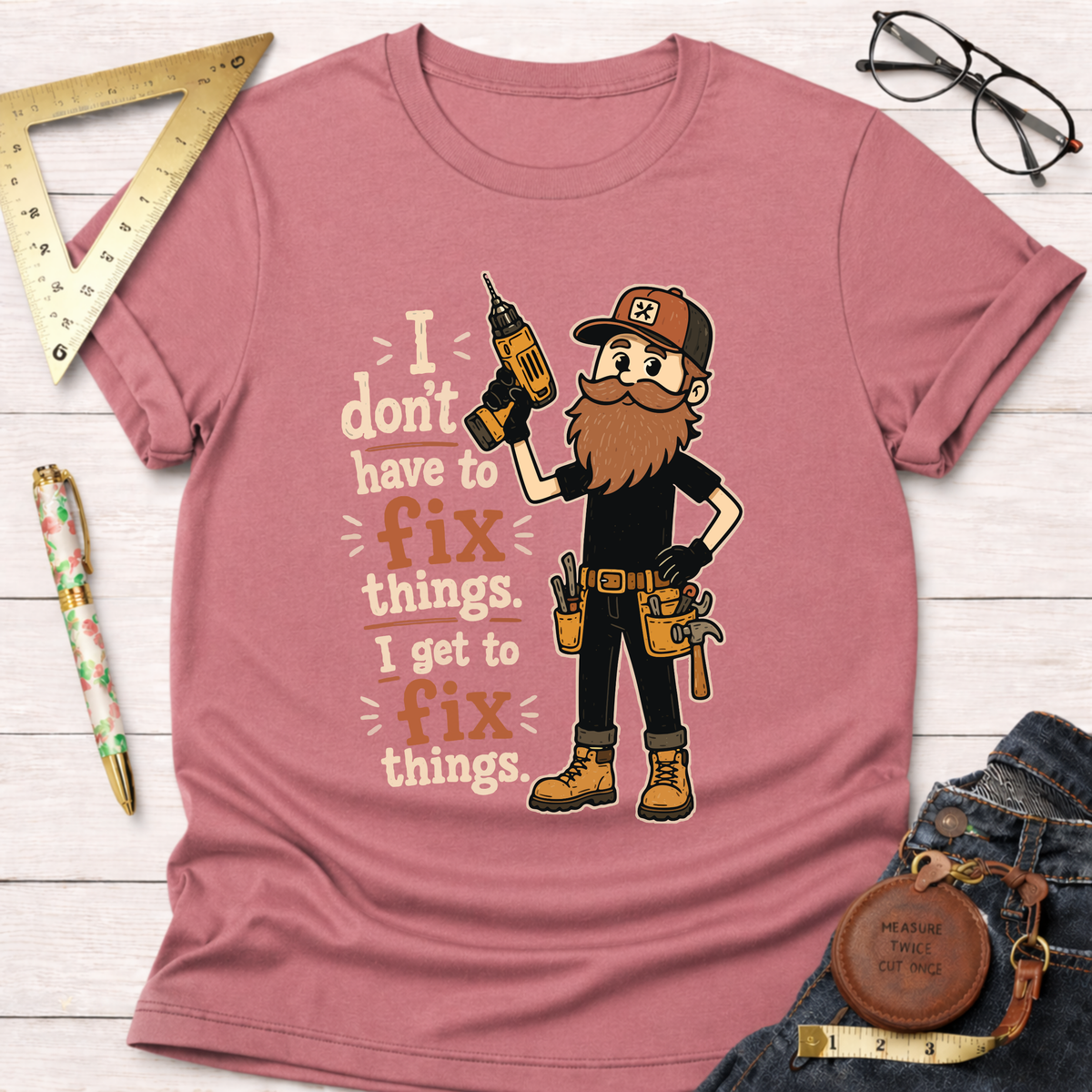 Pink cotton t-shirt with a bearded handyman holding a drill and the text "I don't have to fix things. I get to fix things.