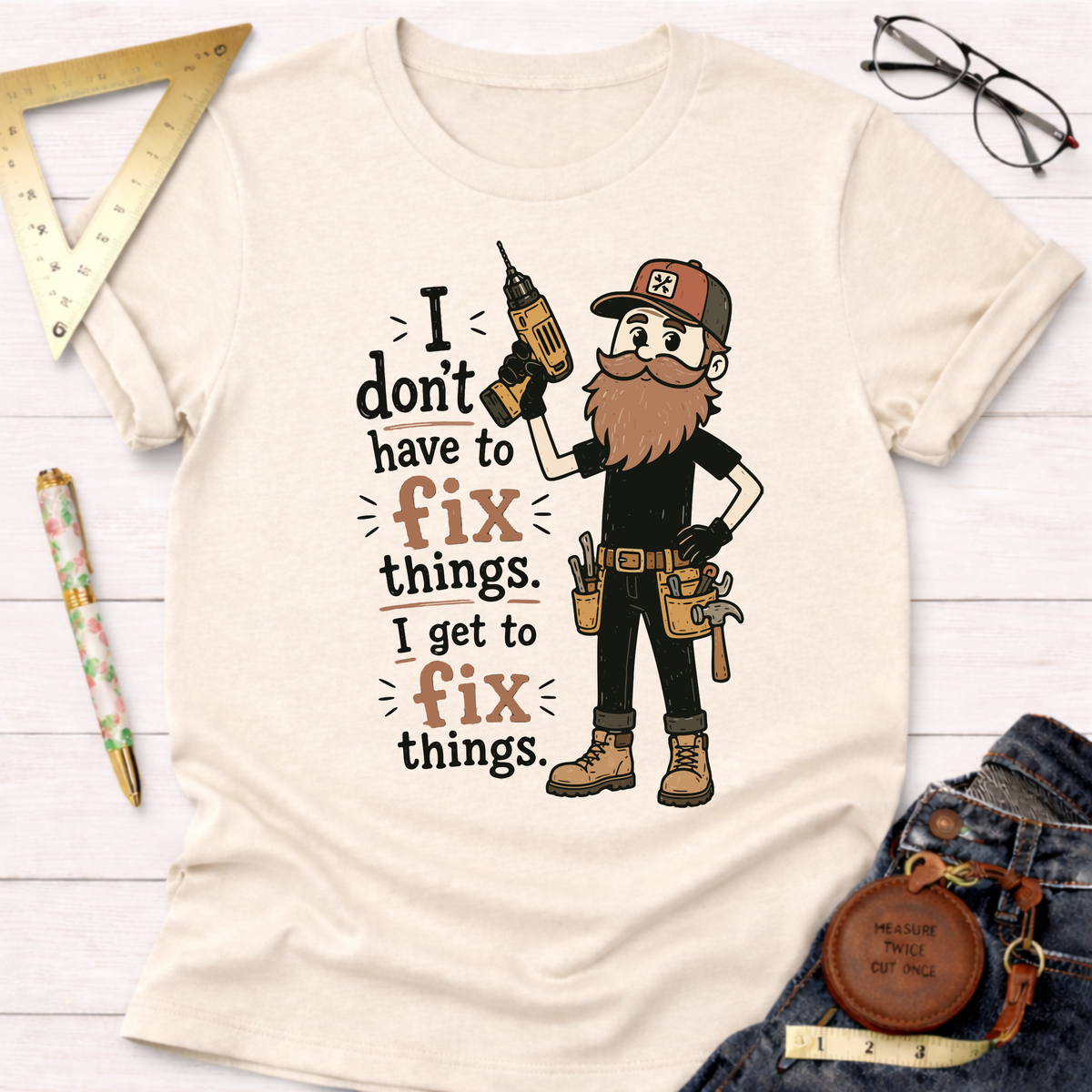Cream cotton t-shirt with a bearded carpenter holding a drill and the text "I don't have to fix things. I get to fix things.