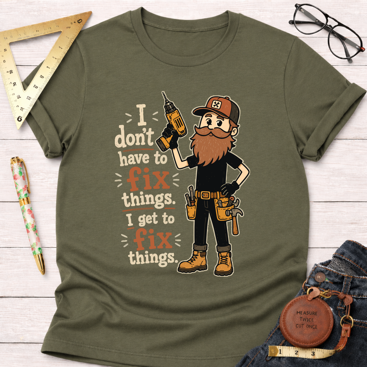 Olive green cotton t-shirt with a cartoon handyman holding a drill and the text "I don't have to fix things. I get to fix things.
