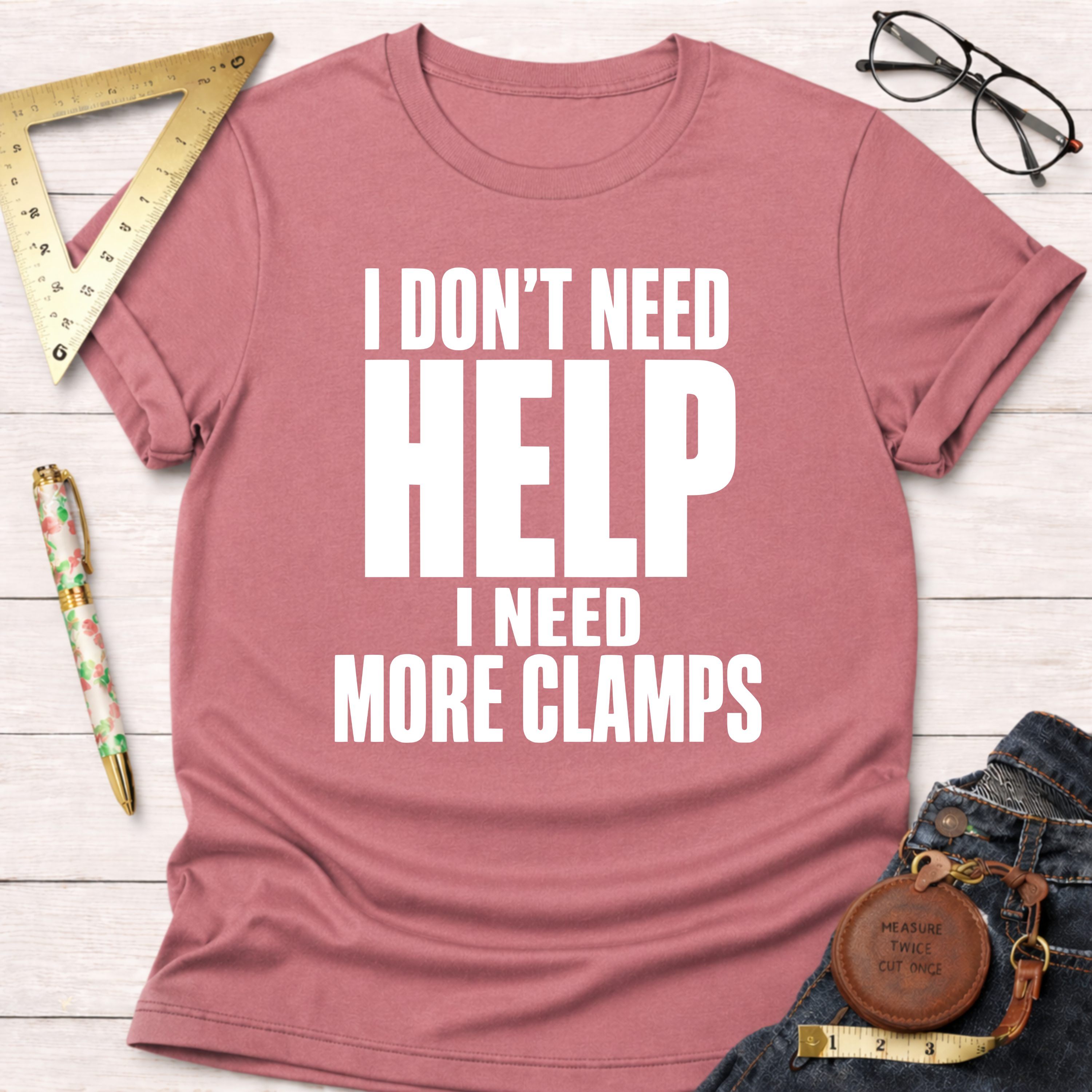 Pink unisex t-shirt with "I DON'T NEED HELP I NEED MORE CLAMPS" in white text.