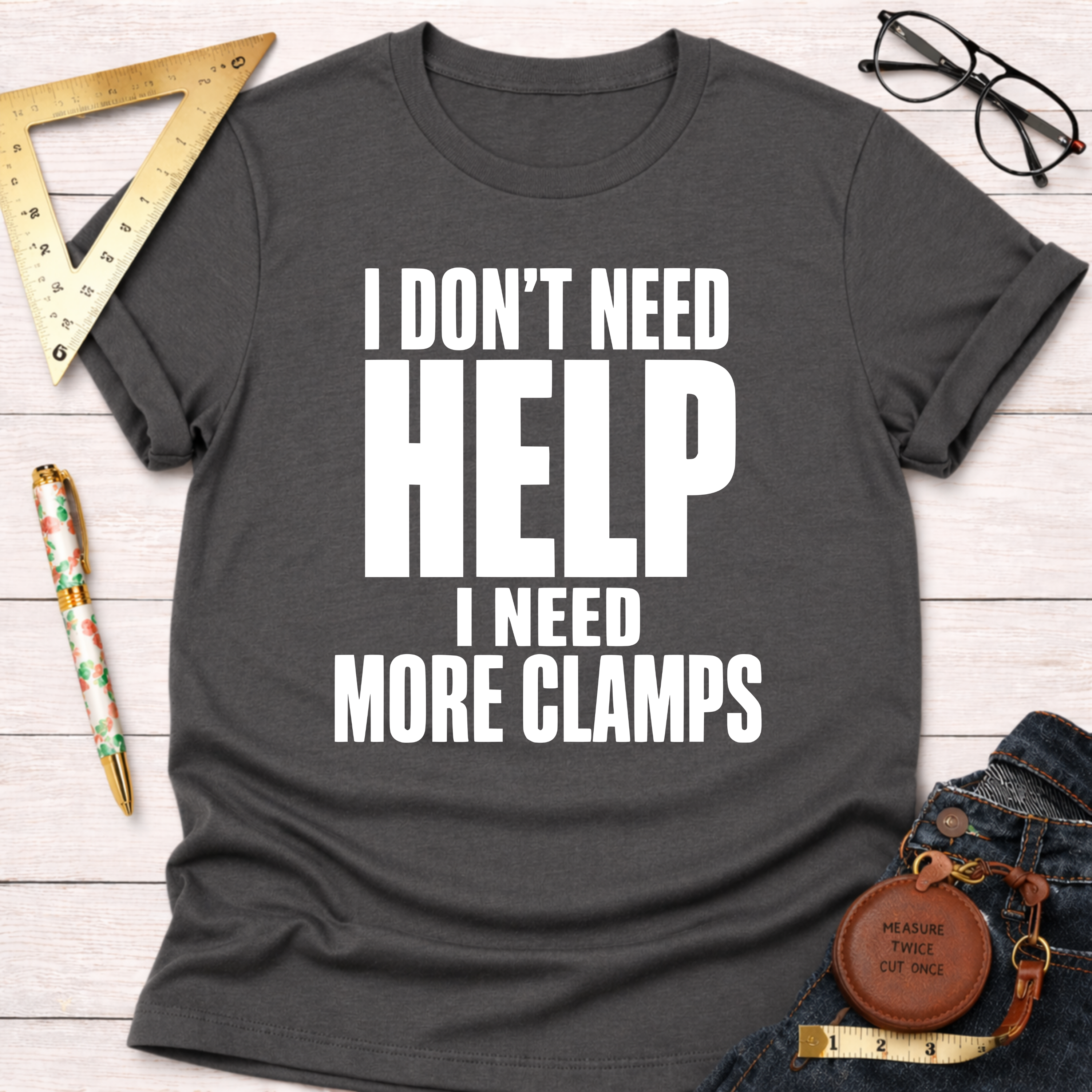 Charcoal grey unisex t-shirt with "I Don't Need Help. I Need More Clamps." in white text.