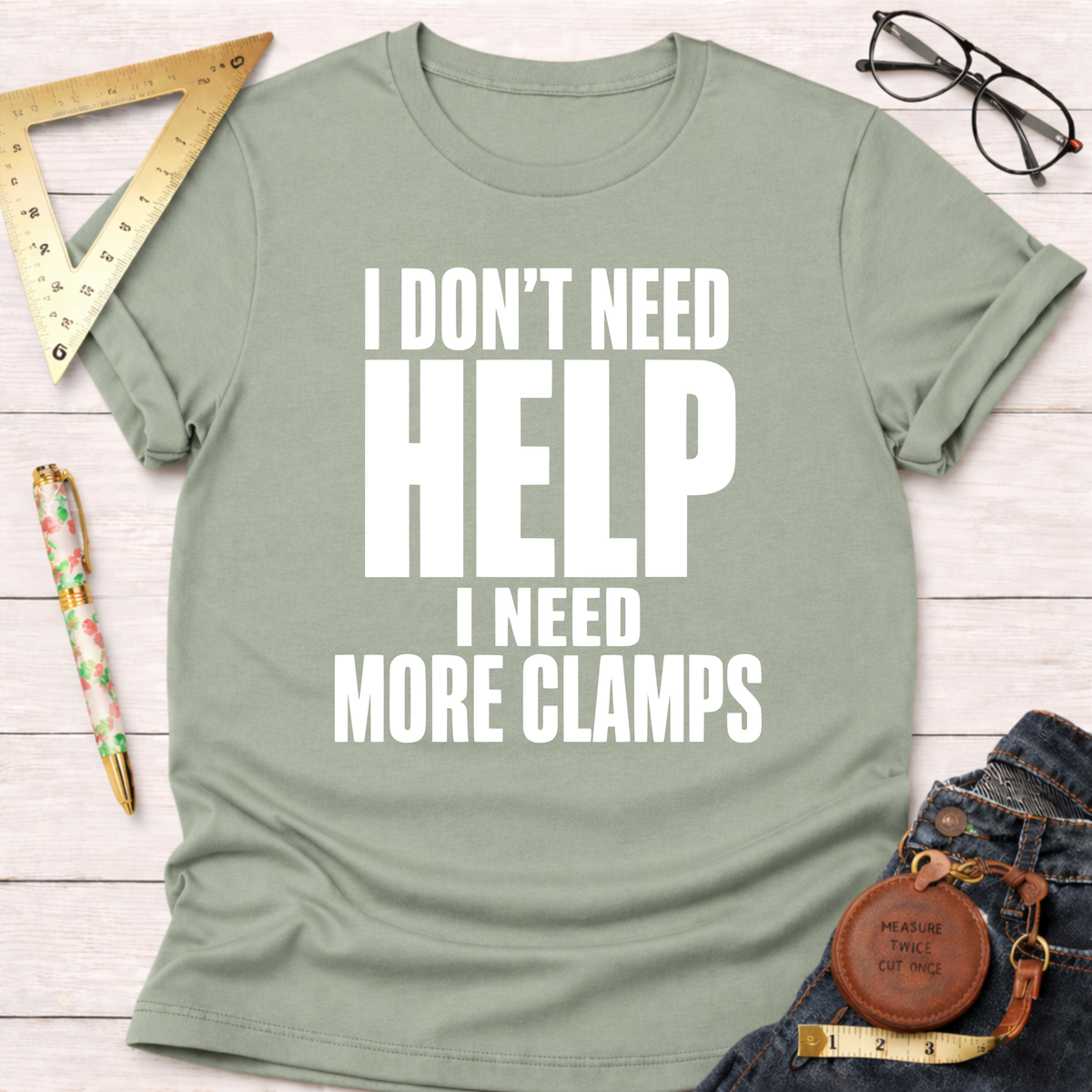 Sage green unisex cotton t-shirt with "I DON'T NEED HELP I NEED MORE CLAMPS" in white text.