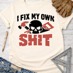 Women's funny woodworking graphic tee shirt for female woodworkers, makers, and DIY builders — Sawdust & Ponytails. Cream t-shirt with "I FIX MY OWN SHIT" text, skull, hammer, and saw graphic.