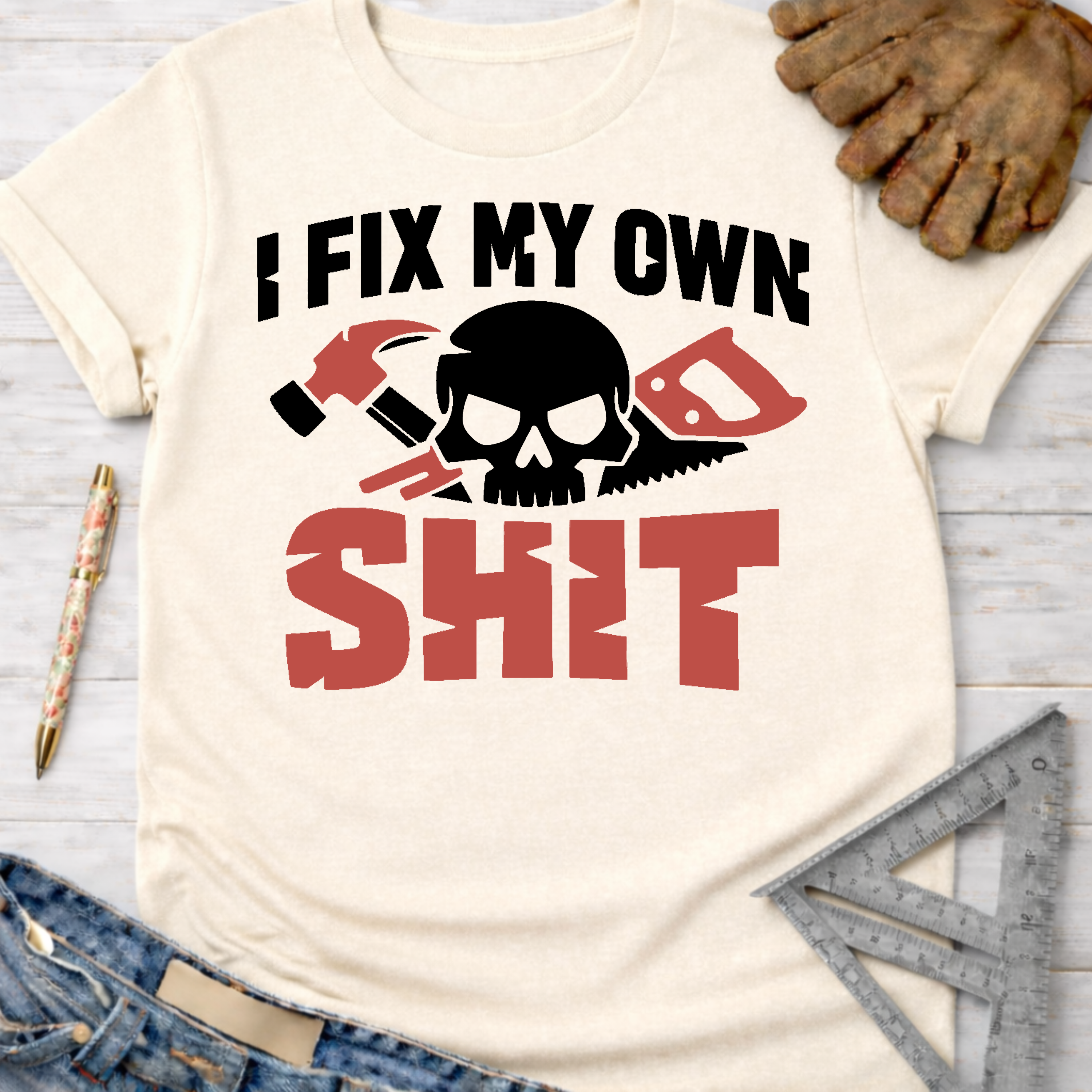 Women's funny woodworking graphic tee shirt for female woodworkers, makers, and DIY builders — Sawdust & Ponytails. Cream t-shirt with "I FIX MY OWN SHIT" text, skull, hammer, and saw graphic.