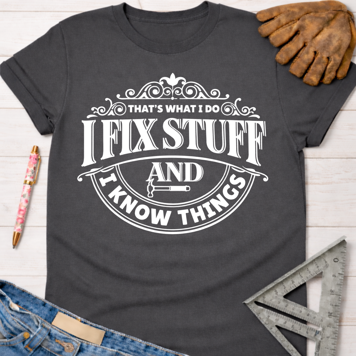 Charcoal gray women's "I Fix Stuff & Know Things" graphic tee, Sawdust & Ponytails, with work glove, jeans, and ruler.