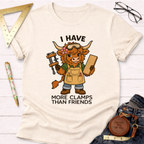 Women's funny woodworking graphic tee shirt for female woodworkers, makers, and DIY builders — Sawdust & Ponytails. Cream t-shirt with a cartoon Highland cow wearing goggles and an apron, holding a clamp and wood, with text "I Have More Clamps Than Friends".