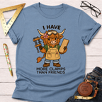 Women's funny woodworking graphic tee shirt for female woodworkers, makers, and DIY builders — Sawdust & Ponytails. Light blue cotton tee with a cartoon highland cow wearing goggles and an apron, holding a clamp and wood, with text "I Have More Clamps Than Friends".