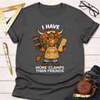 Women's funny woodworking graphic tee shirt for female woodworkers, makers, and DIY builders — Sawdust & Ponytails. Dark gray t-shirt with a cartoon Highland cow wearing safety goggles and an apron, holding a clamp and wood, with the text "I HAVE MORE CLAMPS THAN FRIENDS".