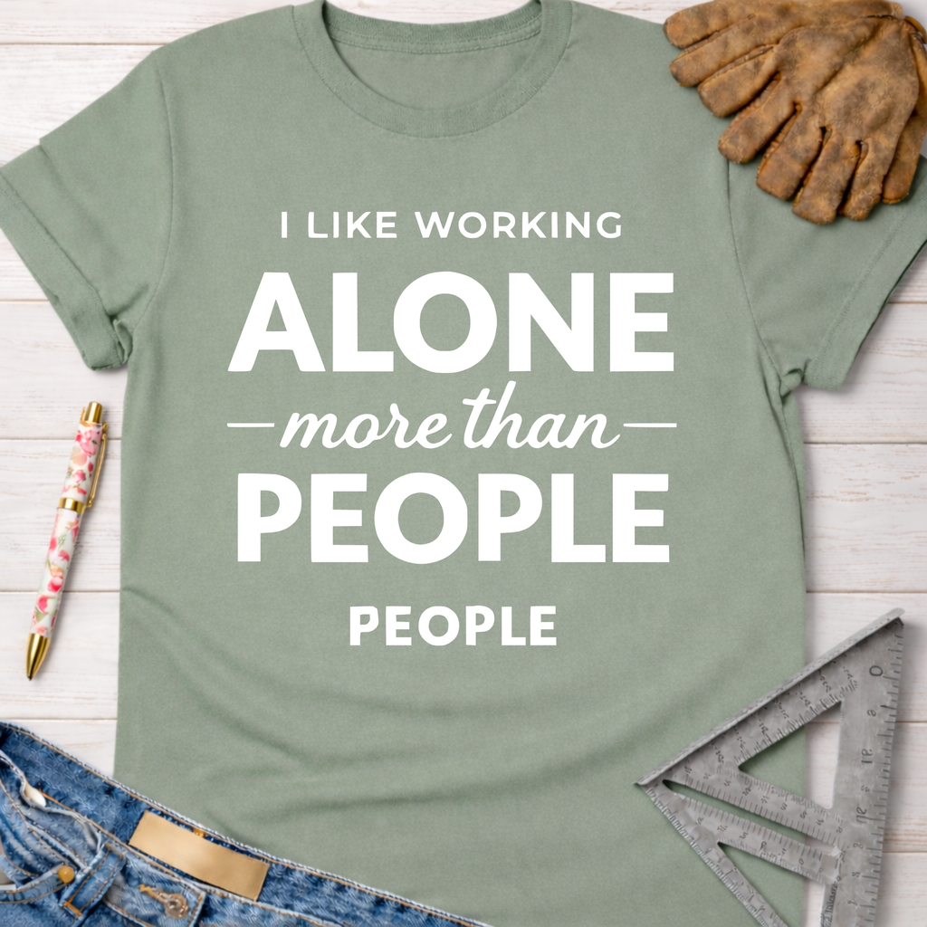 Women's funny woodworking graphic tee shirt for female woodworkers, makers, and DIY builders — Sawdust & Ponytails. Sage green cotton tee with "I LIKE WORKING ALONE more than PEOPLE" in white text, surrounded by work gloves, jeans, and a speed square.