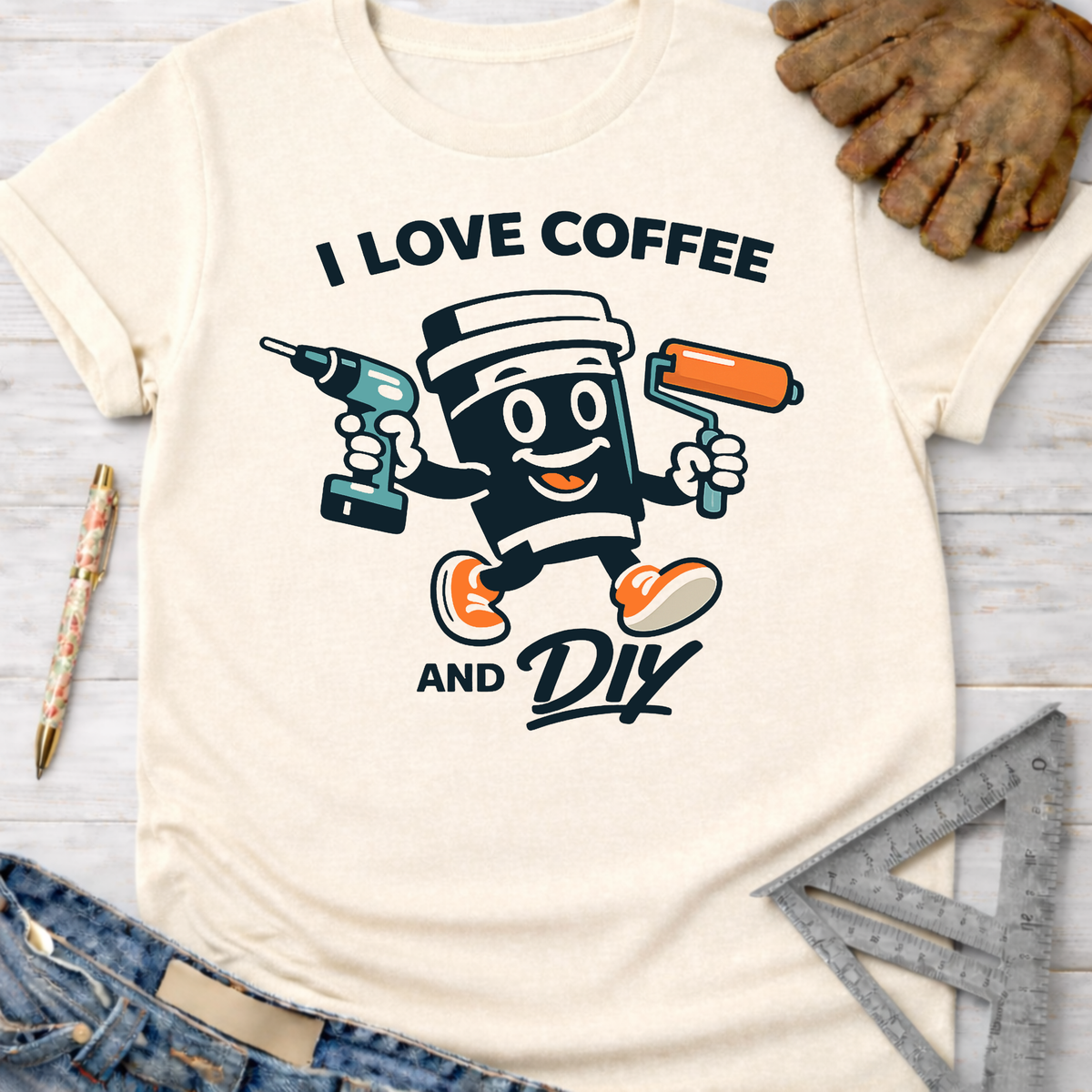 Women's funny woodworking graphic tee shirt for female woodworkers, makers, and DIY builders — Sawdust & Ponytails. Cream t-shirt with "I Love Coffee and DIY" text and a cartoon coffee cup holding a drill and paint roller.