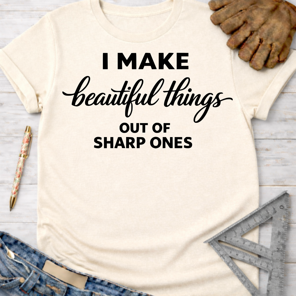 Women's funny woodworking graphic tee shirt for female woodworkers, makers, and DIY builders — Sawdust & Ponytails. Cream t-shirt with "I MAKE beautiful things OUT OF SHARP ONES" in black text.