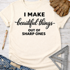 Women's funny woodworking graphic tee shirt for female woodworkers, makers, and DIY builders — Sawdust & Ponytails. Cream t-shirt with "I MAKE beautiful things OUT OF SHARP ONES" in black text.