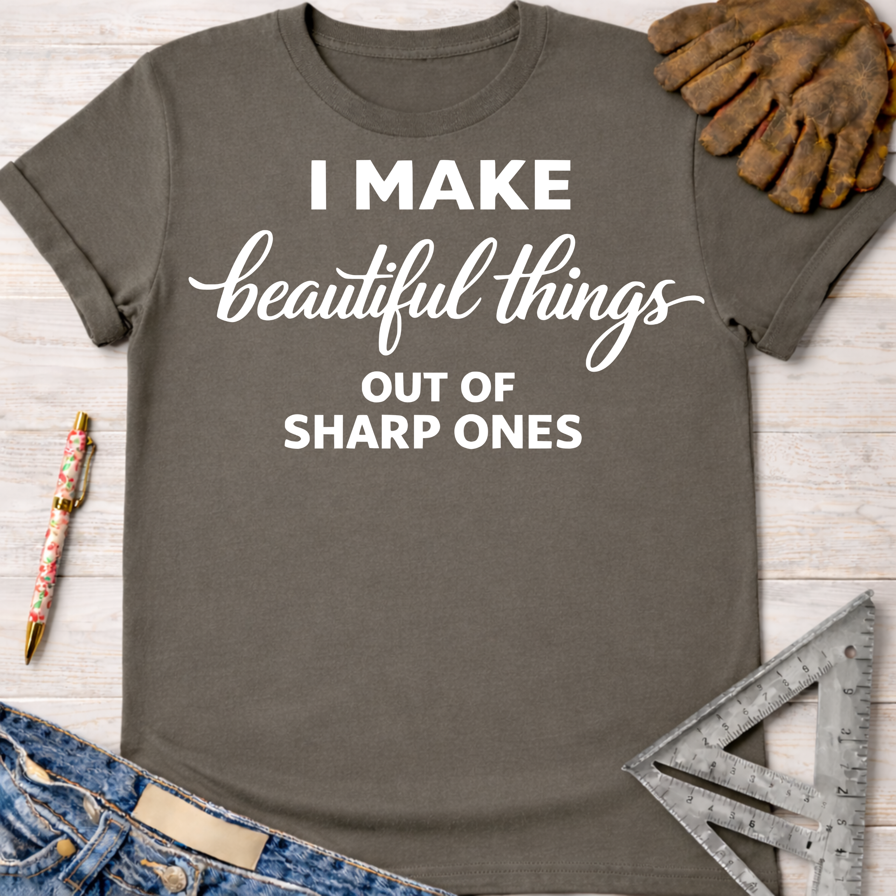 Women's funny woodworking graphic tee shirt for female woodworkers, makers, and DIY builders — Sawdust & Ponytails. Dark gray cotton tee with "I Make beautiful things OUT OF SHARP ONES" in white text, styled with jeans, gloves, and tools.