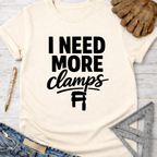 Women's funny woodworking graphic tee shirt for female woodworkers, makers, and DIY builders — Sawdust & Ponytails. Cream t-shirt with "I Need More Clamps" text and clamp graphic.
