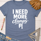 Women's funny woodworking graphic tee shirt for female woodworkers, makers, and DIY builders — Sawdust & Ponytails. Blue cotton t-shirt with "I Need More Clamps" text and clamp graphic.