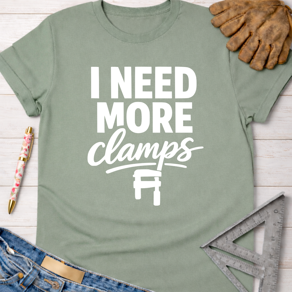 Women's funny woodworking graphic tee shirt for female woodworkers, makers, and DIY builders — Sawdust & Ponytails. Sage green cotton tee with "I NEED MORE clamps" text and clamp graphic.