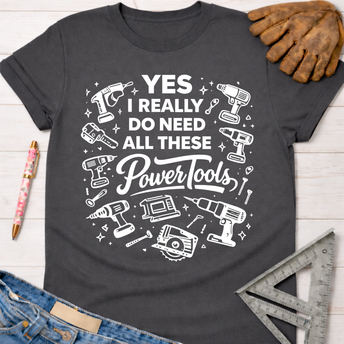 Women's funny woodworking graphic tee shirt for female woodworkers, makers, and DIY builders — Sawdust & Ponytails. Dark gray cotton t-shirt with "YES I REALLY DO NEED ALL THESE Power Tools" in white, surrounded by various power tool illustrations.