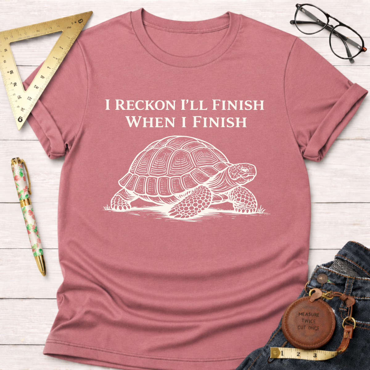 Women's funny woodworking graphic tee shirt for female woodworkers, makers, and DIY builders — Sawdust & Ponytails. Mauve short-sleeve t-shirt with "I Reckon I'll Finish When I Finish" text and a turtle graphic.