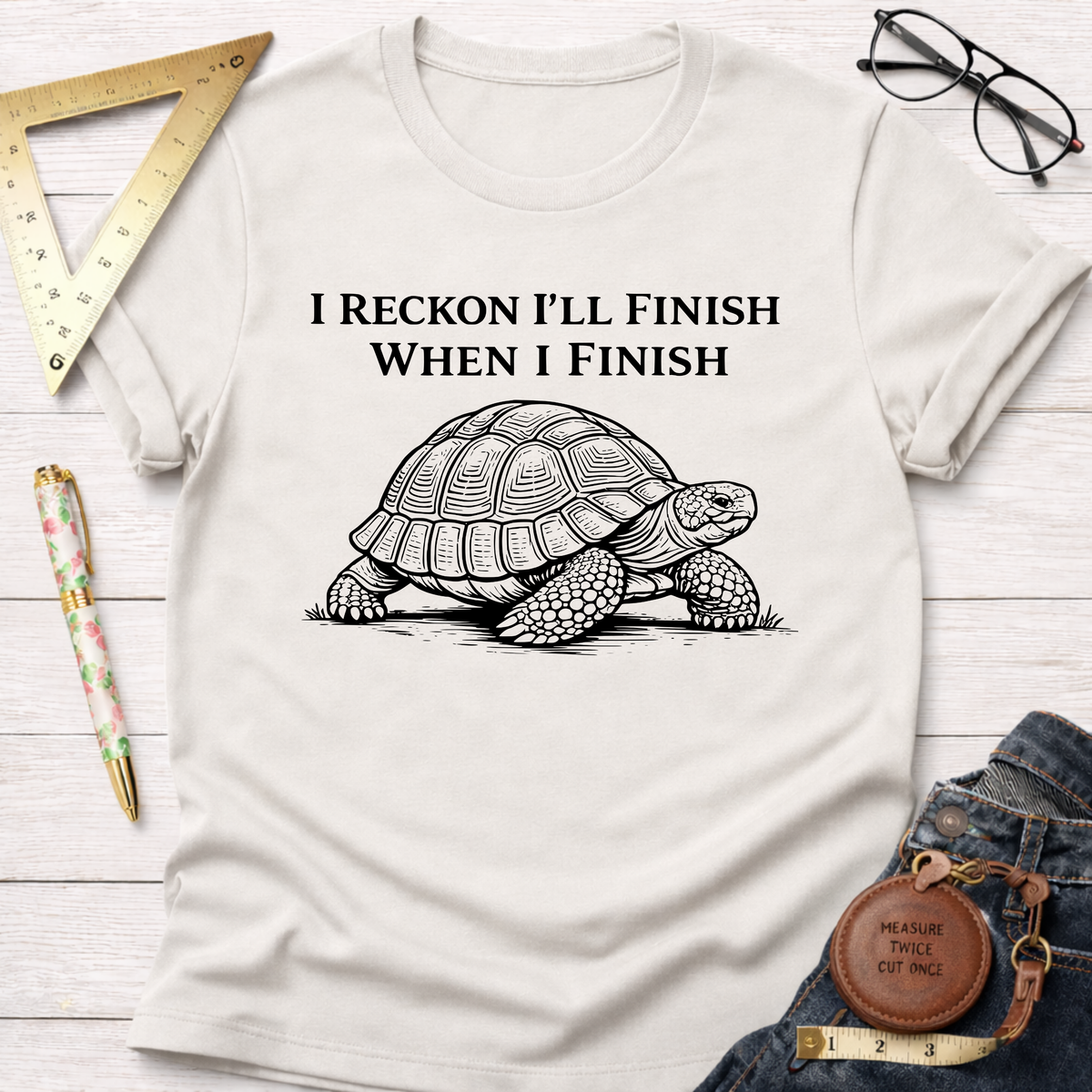 Women's funny woodworking graphic tee shirt for female woodworkers, makers, and DIY builders — Sawdust & Ponytails. Cream t-shirt with "I Reckon I'll Finish When I Finish" text and a detailed turtle graphic.