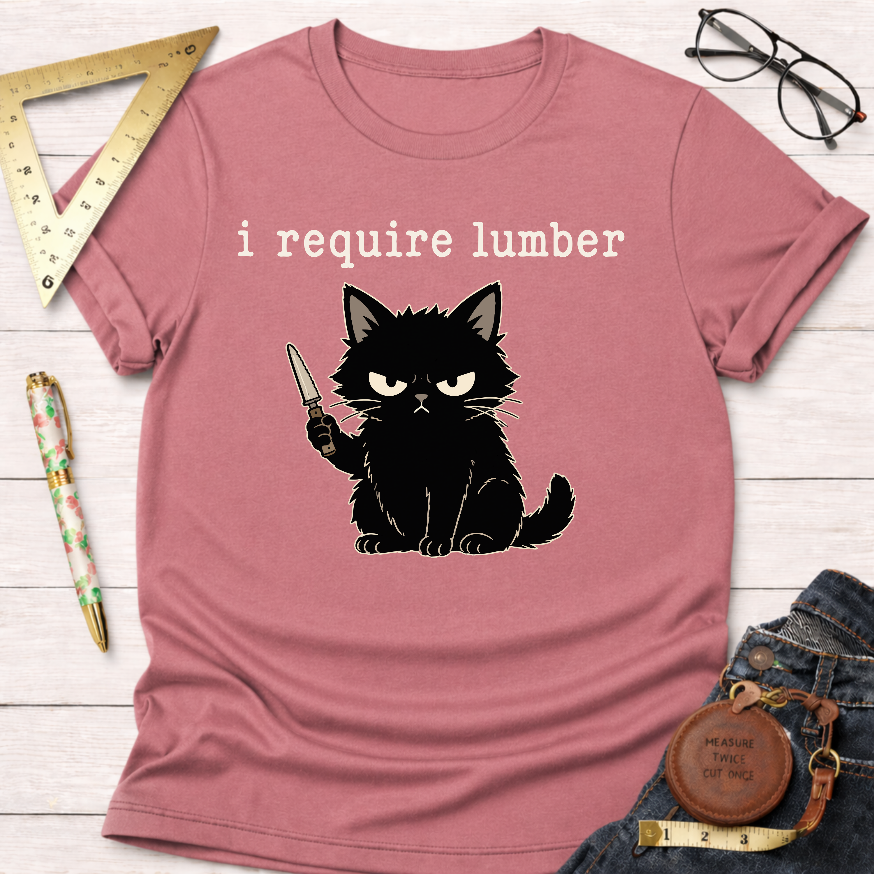 Pink cotton t-shirt with an angry black cat holding a knife and "i require lumber" text.