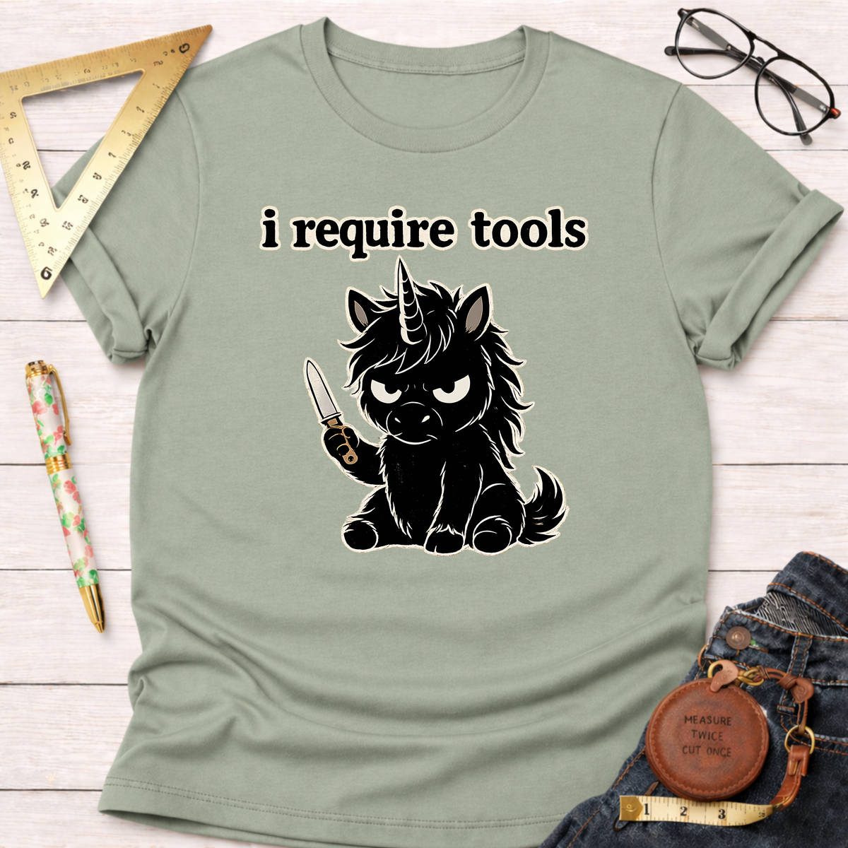Sage green t-shirt with a black angry unicorn holding a knife and "i require tools" text.
