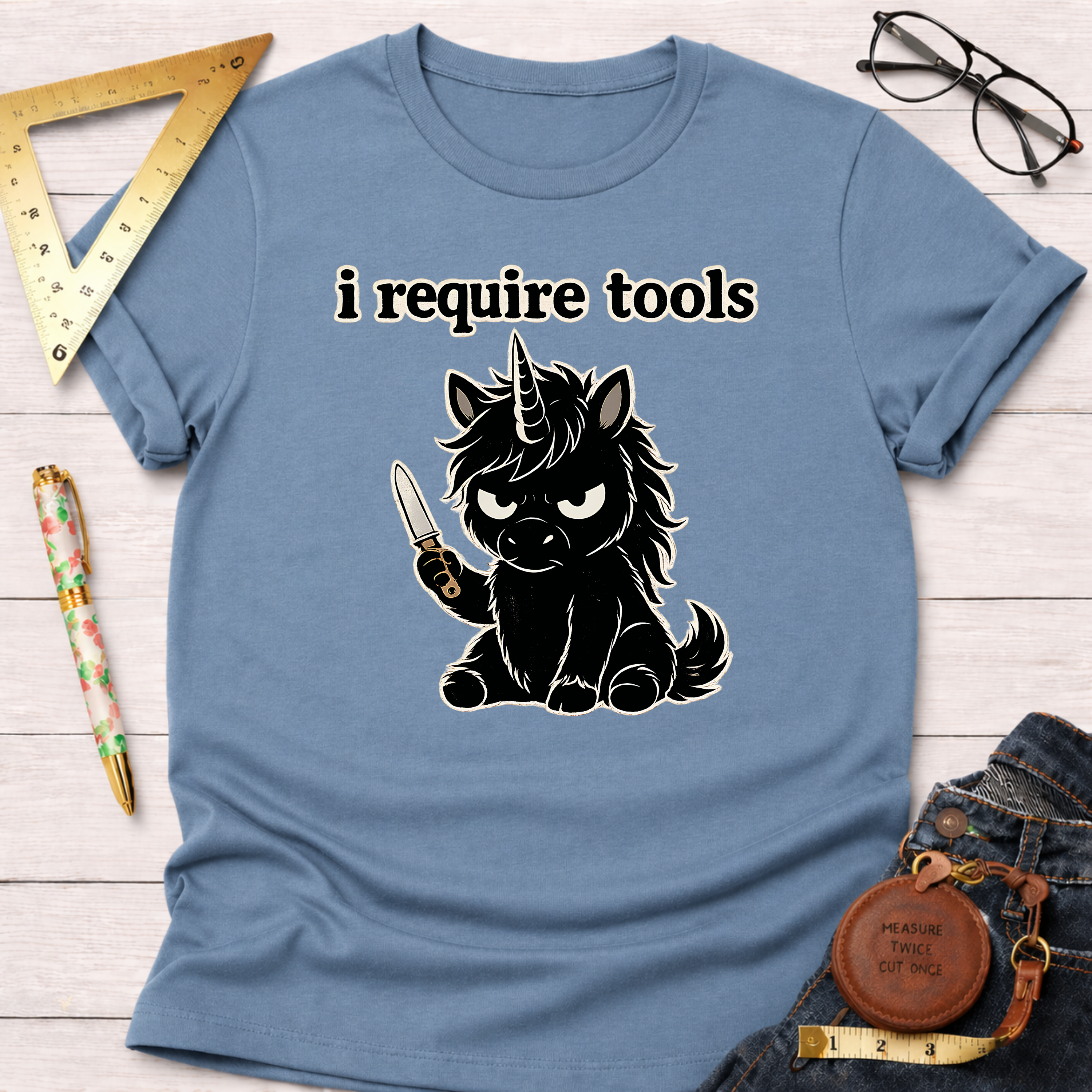 Light blue t-shirt with a black angry unicorn holding a knife and "i require tools" text.