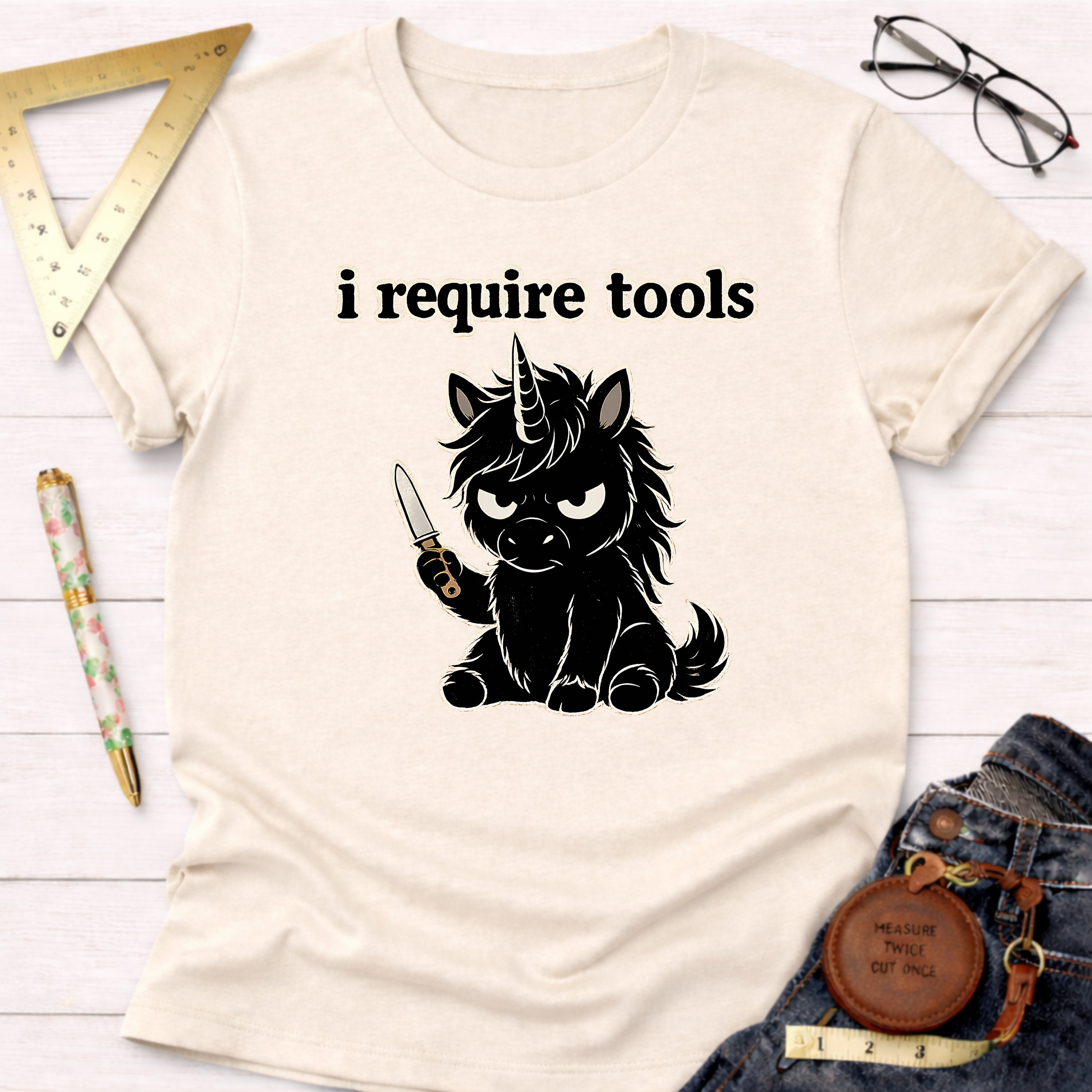 Cream t-shirt with "i require tools" and an angry black unicorn holding a knife.