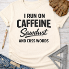 Women's funny woodworking graphic tee shirt for female woodworkers, makers, and DIY builders — Sawdust & Ponytails. Cream t-shirt with "I RUN ON CAFFEINE Sawdust AND CUSS WORDS" in black text.