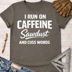 Women's funny woodworking graphic tee shirt for female woodworkers, makers, and DIY builders — Sawdust & Ponytails. Dark gray cotton tee with "I RUN ON CAFFEINE Sawdust AND CUSS WORDS" in white text.