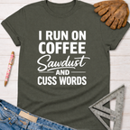 Women's funny woodworking graphic tee shirt for female woodworkers, makers, and DIY builders — Sawdust & Ponytails. Dark gray t-shirt with "I RUN ON COFFEE Sawdust AND CUSS WORDS" in white text.