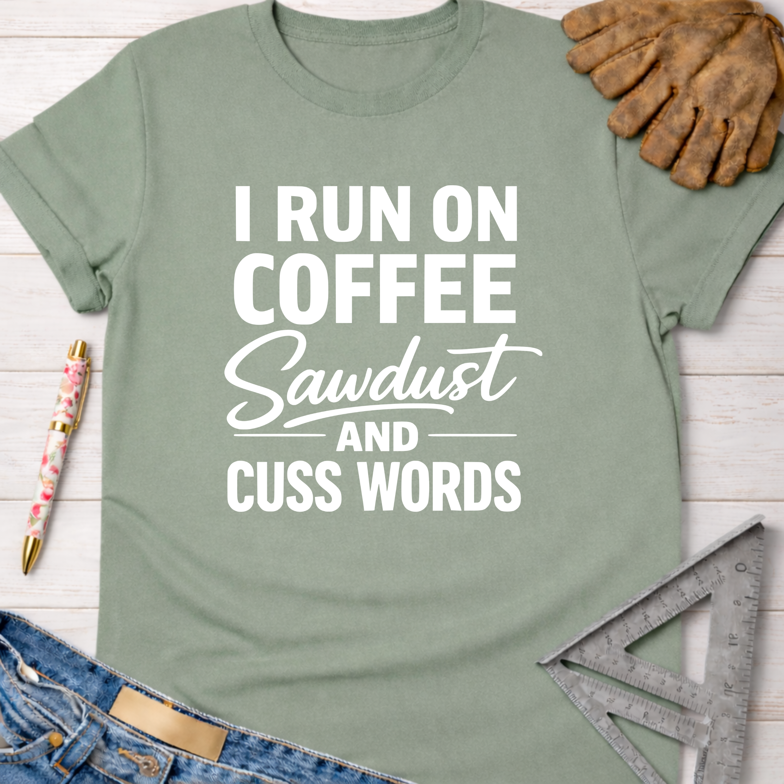 Women's funny woodworking graphic tee shirt for female woodworkers, makers, and DIY builders — Sawdust & Ponytails. Sage green cotton tee with "I RUN ON COFFEE SAWDUST AND CUSS WORDS" in white text.