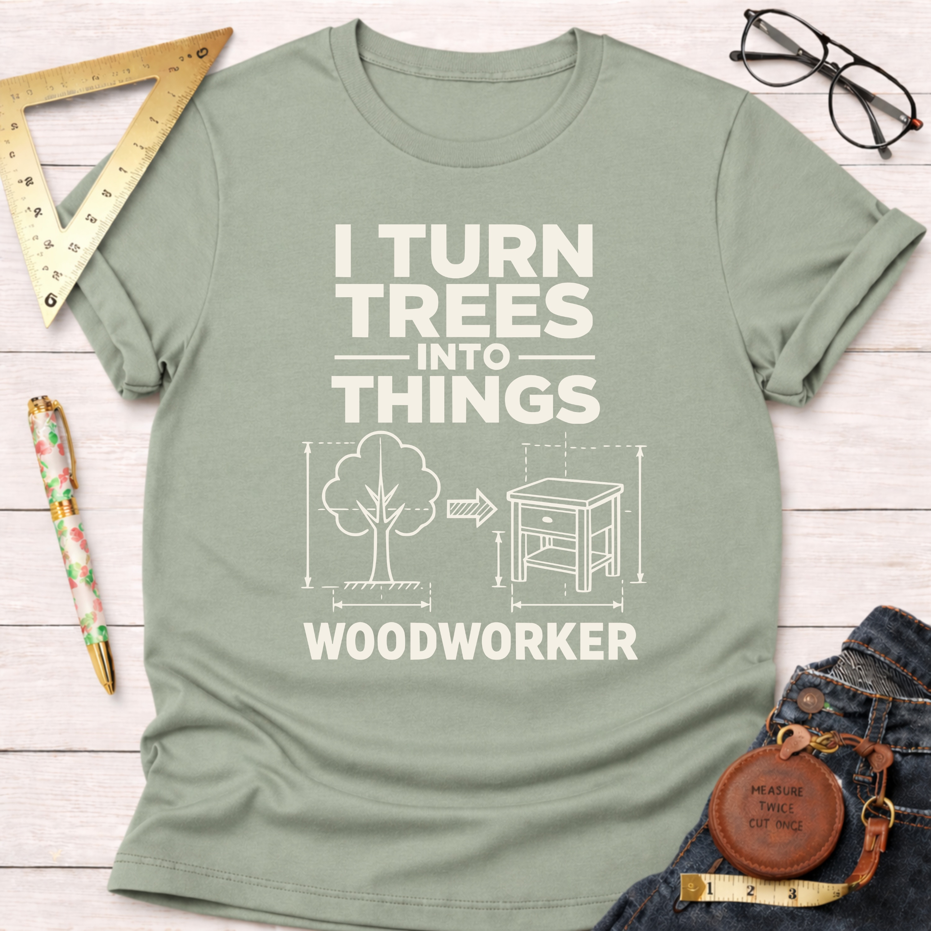 Sage green cotton "I Turn Trees Into Things Woodworker" t-shirt with a tree and furniture graphic.
