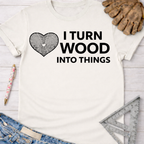 Women's funny woodworking graphic tee shirt for female woodworkers, makers, and DIY builders — Sawdust & Ponytails. Cream short-sleeve tee with "I Turn Wood Into Things" text and a heart-shaped wood grain graphic.