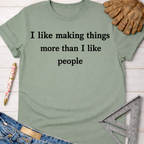 Women's funny woodworking graphic tee shirt for female woodworkers, makers, and DIY builders — Sawdust & Ponytails. Sage green cotton tee with "I like making things more than I like people" text.
