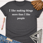 Women's funny woodworking graphic tee shirt for female woodworkers, makers, and DIY builders — Sawdust & Ponytails. Dark gray cotton t-shirt with "I like making things more than I like people" in white text.