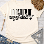 Women's funny woodworking graphic tee shirt for female woodworkers, makers, and DIY builders — Sawdust & Ponytails. Cream t-shirt with "I'd Rather Be Woodworking" in black text.