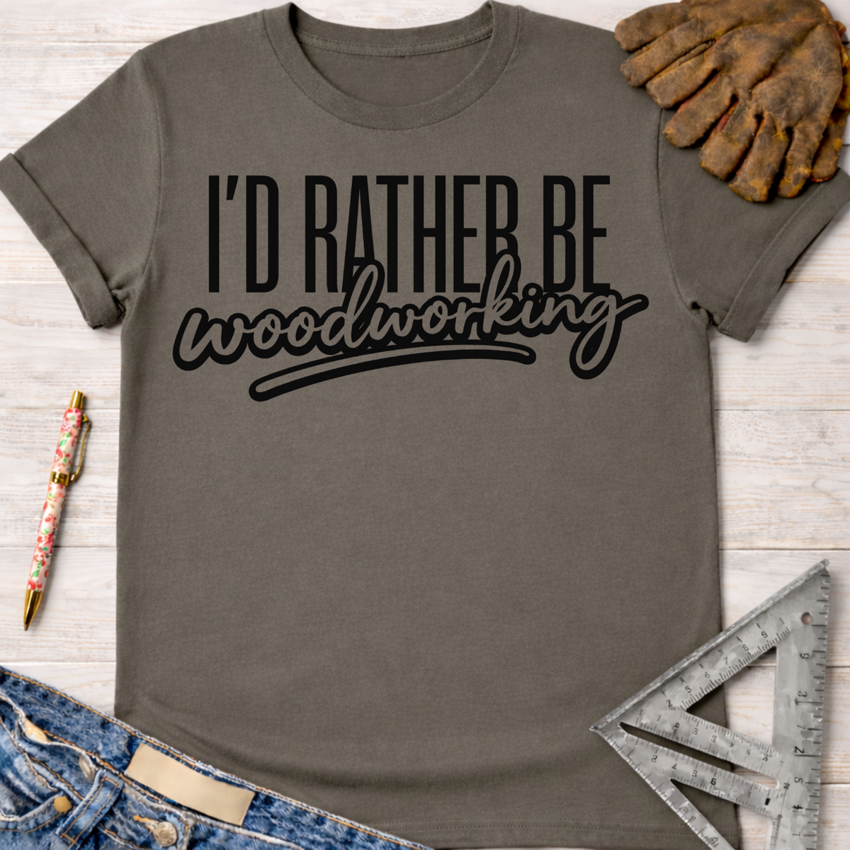 Women's funny woodworking graphic tee shirt for female woodworkers, makers, and DIY builders — Sawdust & Ponytails. Dark gray cotton tee with "I'd Rather Be Woodworking" in black text.