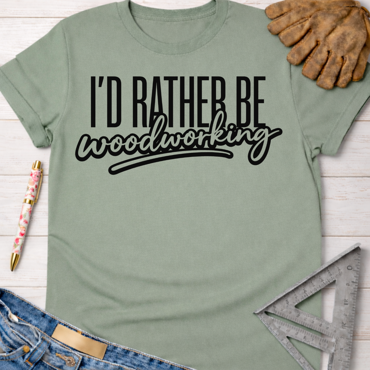 Women's funny woodworking graphic tee shirt for female woodworkers, makers, and DIY builders — Sawdust & Ponytails. Sage green cotton tee with "I'd Rather Be Woodworking" in black text.