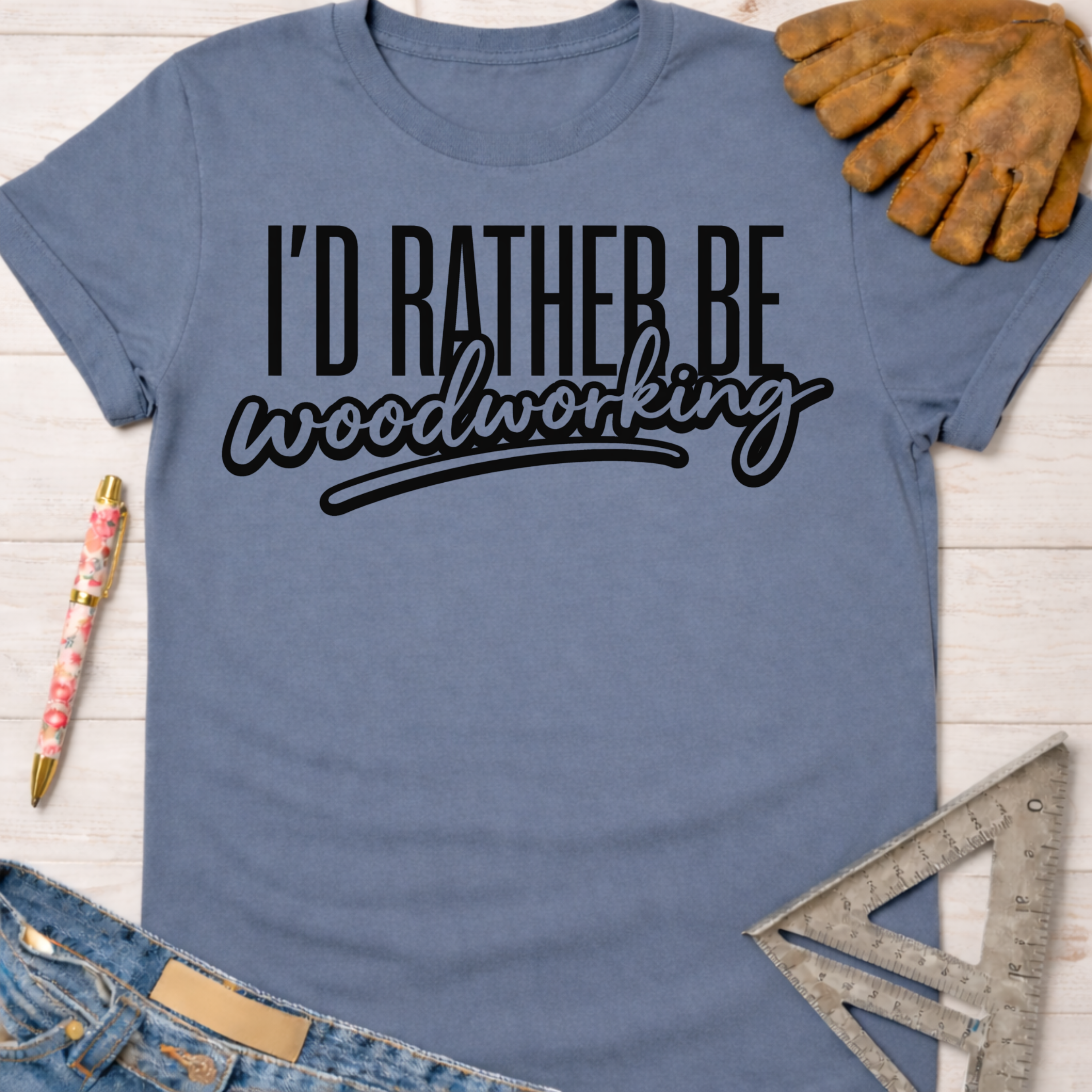 Women's funny woodworking graphic tee shirt for female woodworkers, makers, and DIY builders — Sawdust & Ponytails. Blue cotton tee with "I'd Rather Be Woodworking" in black text.