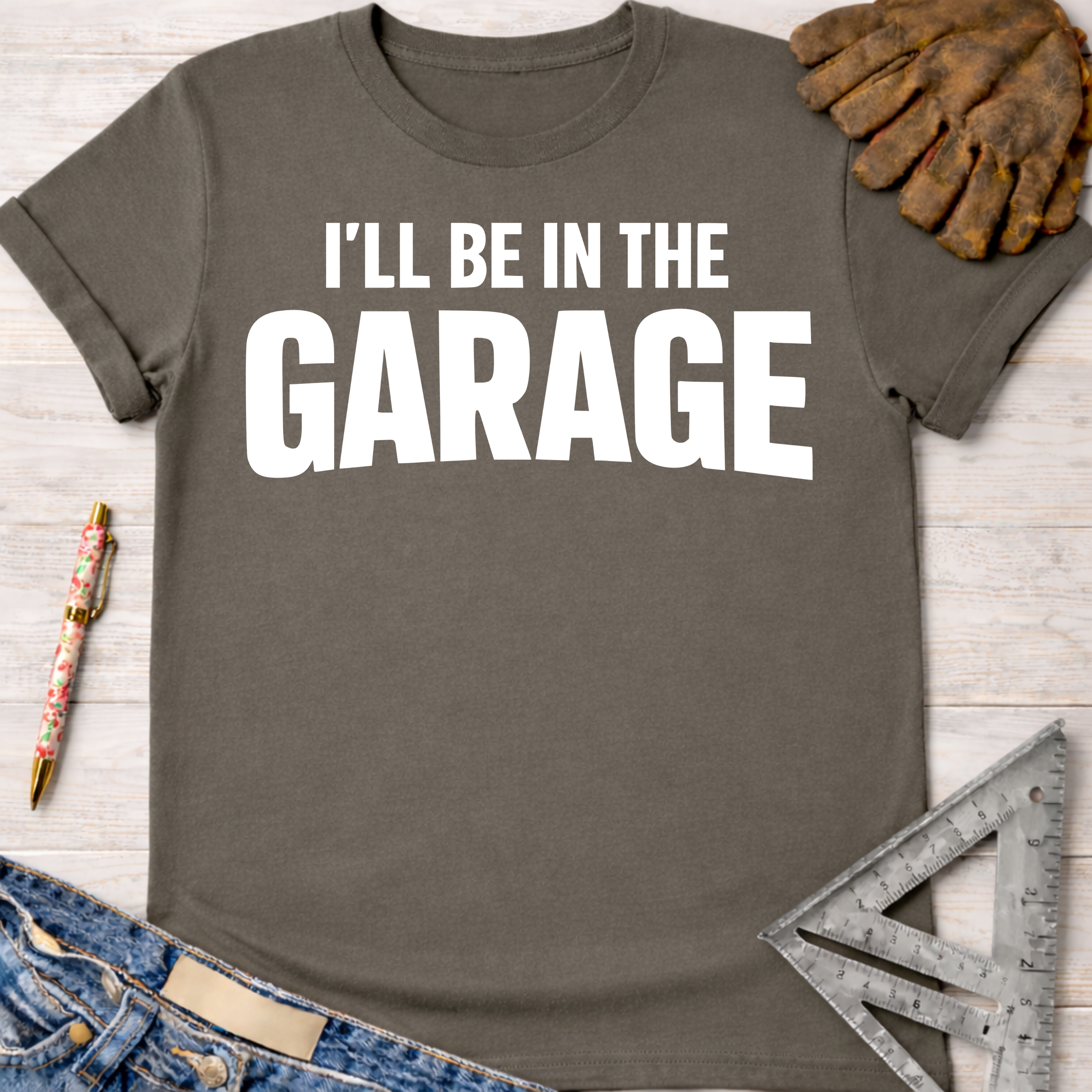 Charcoal grey "I'll Be In The Garage" t-shirt with rolled sleeves, jeans, work gloves, and tools. Women's funny woodworking graphic tee shirt for female woodworkers, makers, and DIY builders — Sawdust & Ponytails