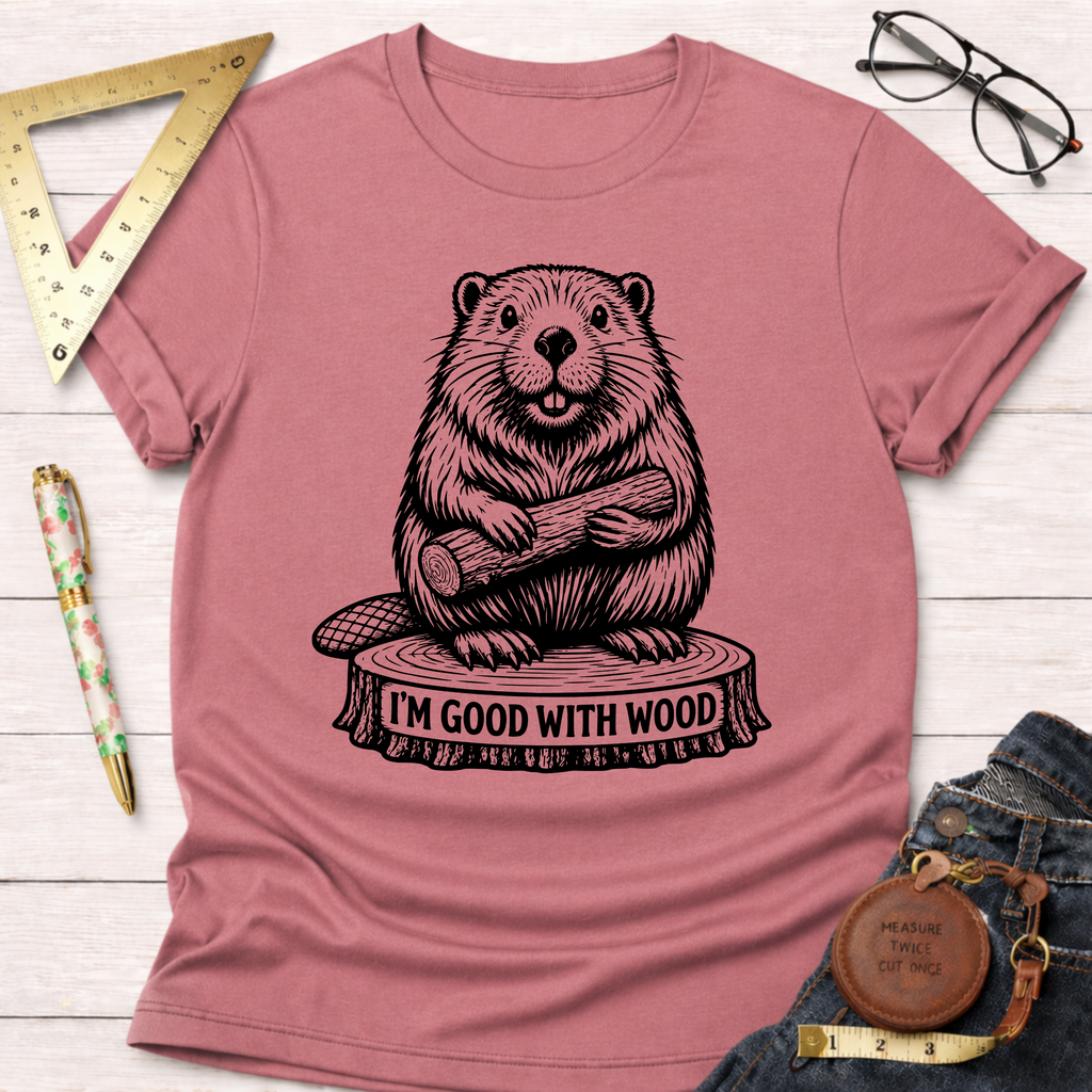 Women's funny woodworking graphic tee shirt for female woodworkers, makers, and DIY builders — Sawdust & Ponytails. Mauve t-shirt with a black beaver graphic holding wood on a tree stump that says "I'm Good With Wood.