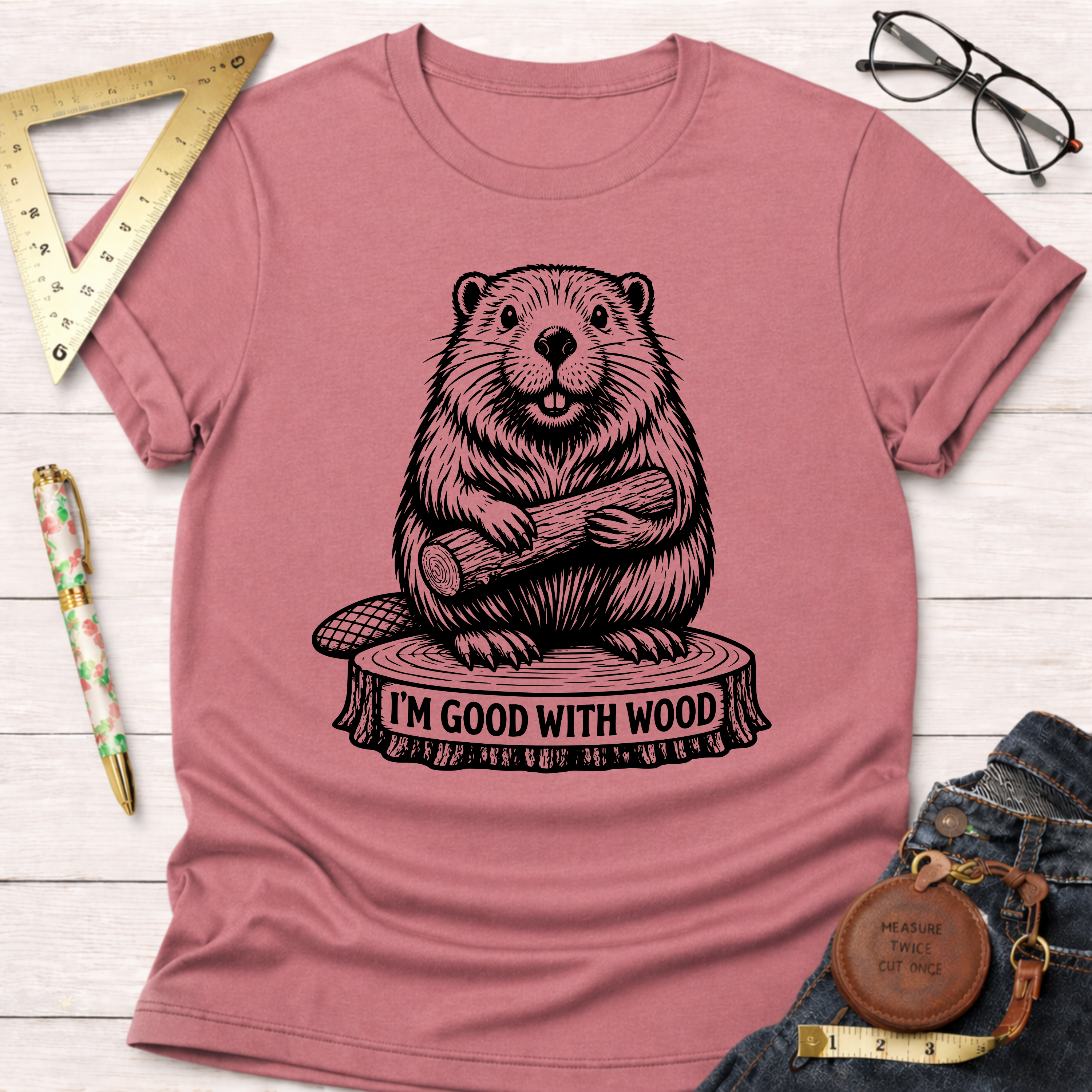 Women's funny woodworking graphic tee shirt for female woodworkers, makers, and DIY builders — Sawdust & Ponytails. Mauve t-shirt with a black beaver graphic holding wood on a tree stump that says "I'm Good With Wood.